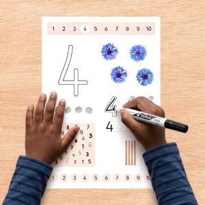 Mains d’un enfant traçant un chiffre avec un feutre effaçable sur une fiche pour apprendre le chiffre 4